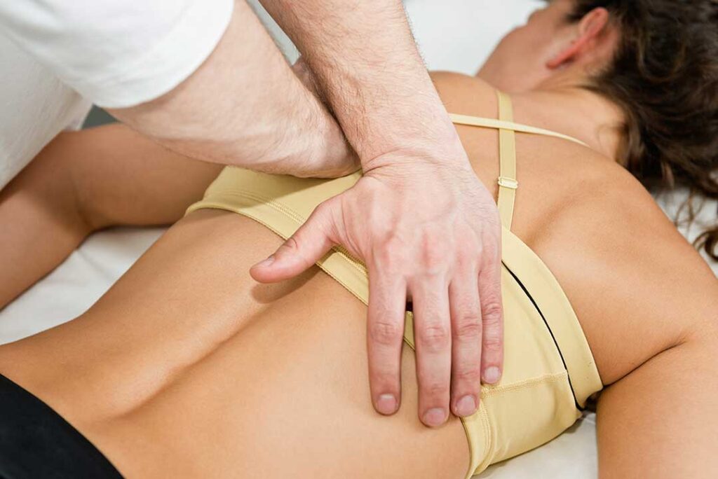 A person receives a gentle spinal adjustment on a treatment table in a warmly lit clinic.